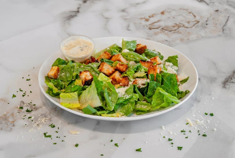 Fresh Caesar salad with crisp romaine, croutons, parmesan, and creamy dressing on a white plate.