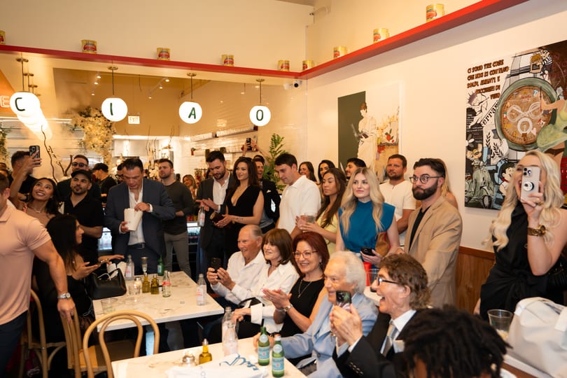 A lively crowd of people, some seated and some standing, enjoying an event in a restaurant.