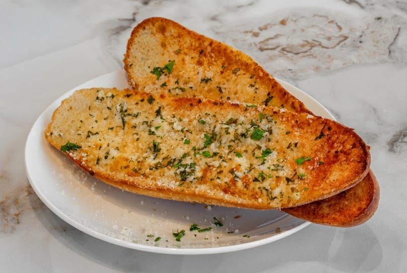 Two slices of golden-brown garlic bread with parsley and parmesan cheese on a white plate.