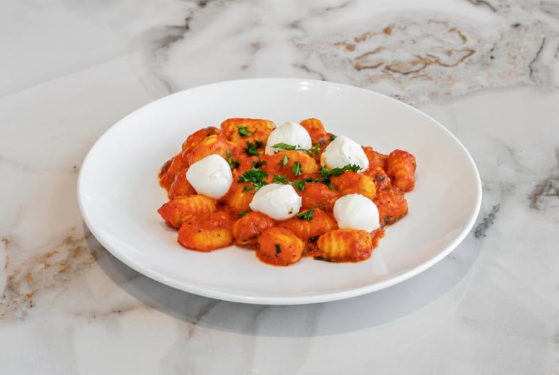 Gnocchi with red sauce, fresh mozzarella balls, and parsley on a white plate.